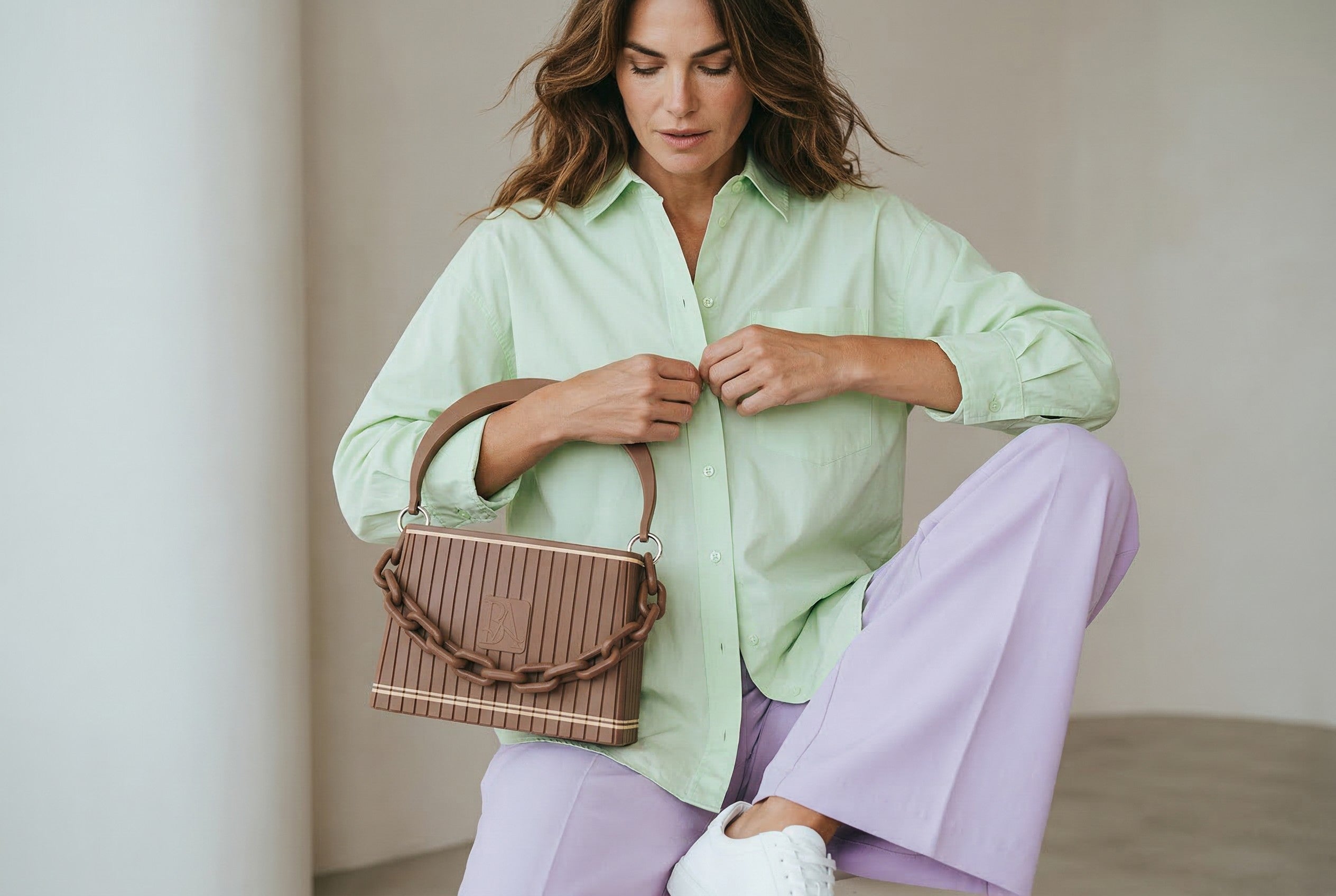 Model trägt HAKO Handtasche in Braun mit Ketten-Detail, moderner Lifestyle-Look im minimalistischen Studio