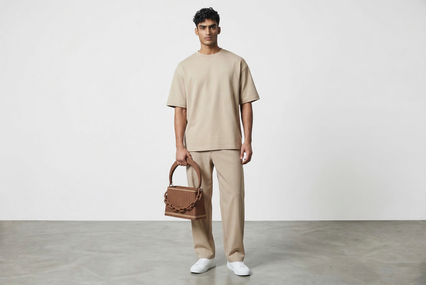 Model trägt HAKO Handtasche in Braun mit Ketten-Detail, moderner unisex Lifestyle-Look im minimalistischen Studio