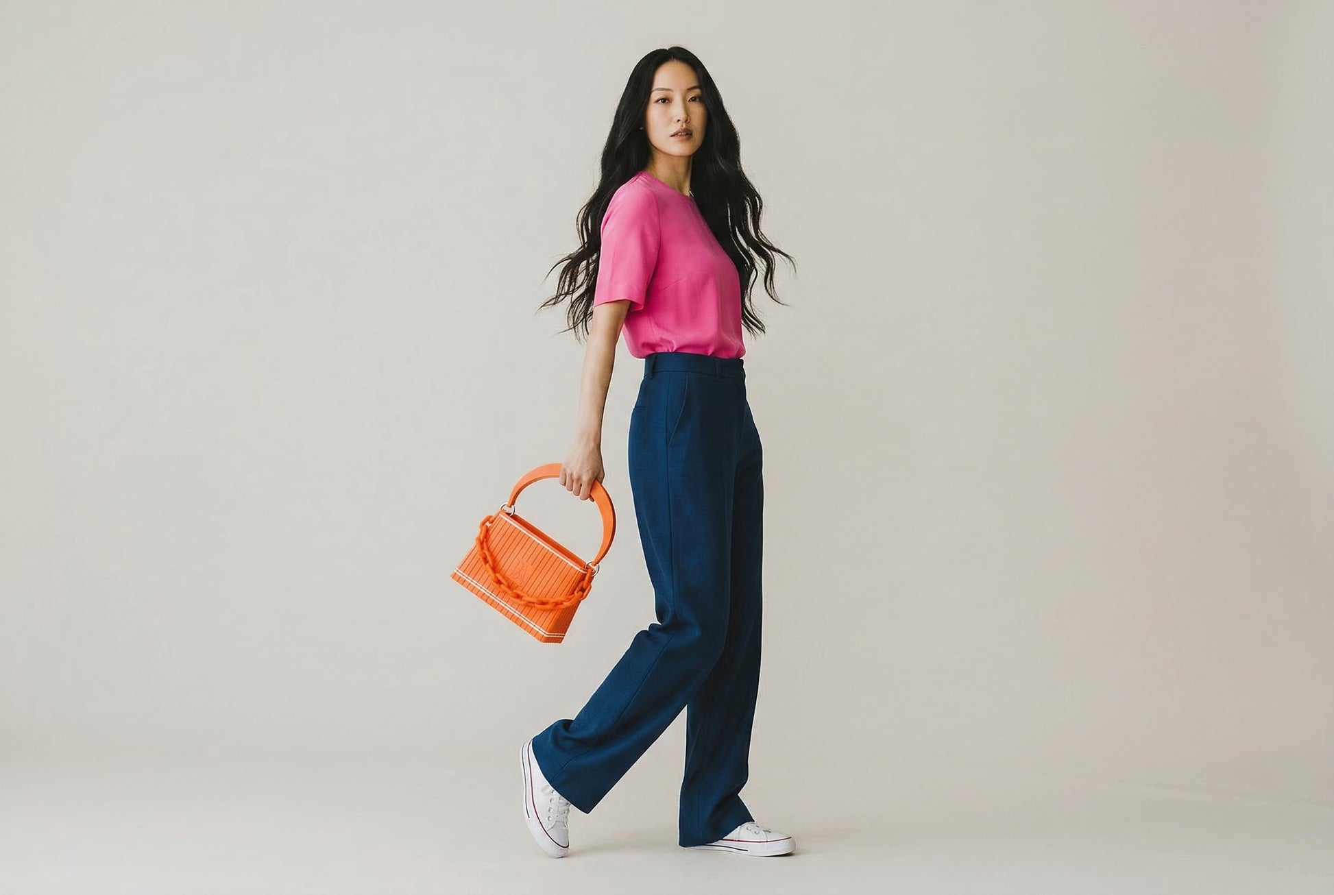 Model trägt HAKO Handtasche in Orange mit Ketten-Detail, moderner Lifestyle-Look im minimalistischen Studio