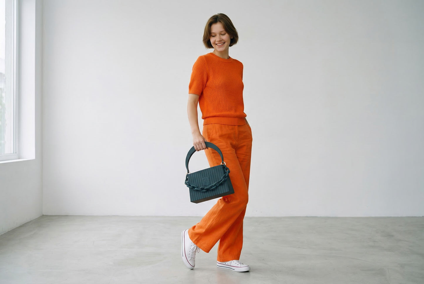 Model trägt HAKO Handtasche in Schwarz mit Ketten-Detail, moderner Lifestyle-Look im minimalistischen Studio